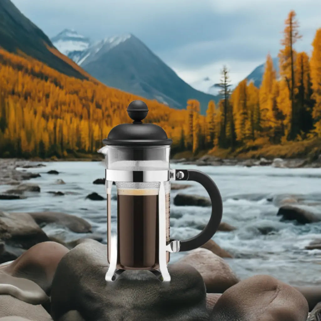 Brew-itCafe French press coffee maker placed on rocks by a serene river surrounded by autumn mountains